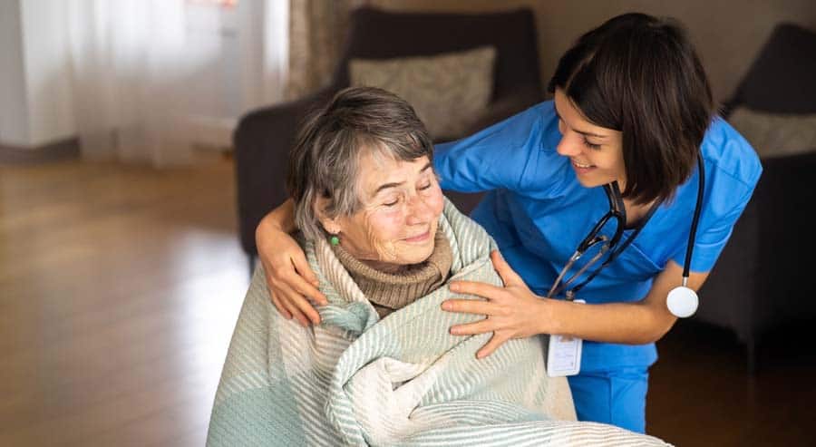 nurse wrapping blanket around elderly female patient